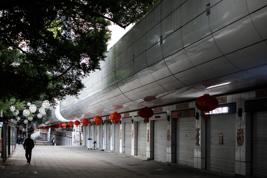 Covered pedestrian walkway with shuttered storefronts and red lantern decorations under a massive concrete overhang.
