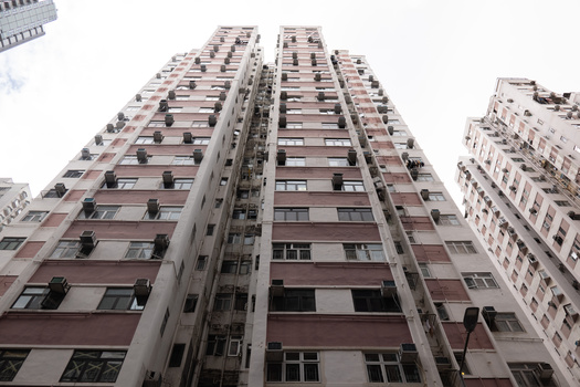 Tall residential apartment building photographed from ground level looking upward against white sky.