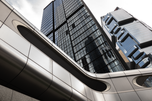 Modern skyscraper facades shot from below, with curved architectural elements framing towering glass and steel buildings against cloudy sky.