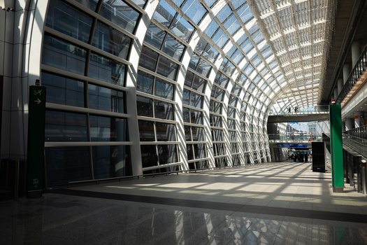 Modern corridor with geometric glass and metal architecture bathed in natural light from above.