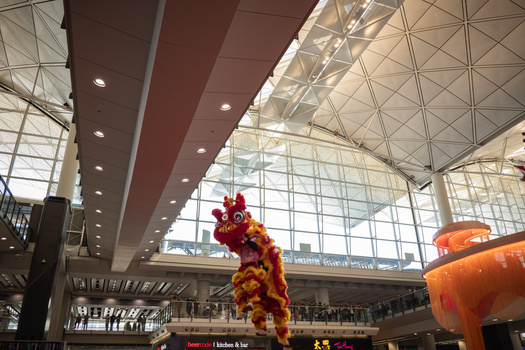 Modern airport terminal interior with geometric glass ceiling, red and yellow floral decoration, and recessed lighting.
