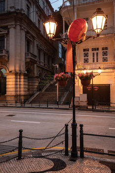 Historic stone building facade at dusk with illuminated street lamp and red balloon decoration.