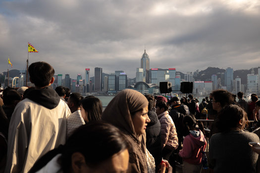 Crowd of people viewing a city skyline across a waterfront during overcast afternoon light.