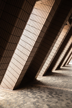 Strong geometric shadows cast through corrugated metal panels onto a textured floor.