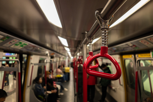 Red handholds hanging from chains inside a transit train car with blurred passengers in the background.