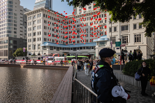 Waterfront plaza with modern and historic architecture, crowds of people, and red lantern decorations on a building.