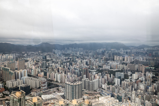 Dense urban skyline with high-rise buildings under overcast skies and mountains in the distance.