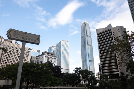 Tall modern skyscraper rises above surrounding mid-rise buildings in an urban downtown district.