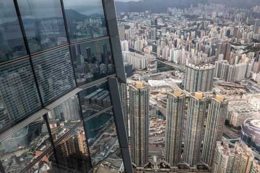 View from high-rise window overlooking dense urban cityscape with numerous residential towers and mountains in distance.