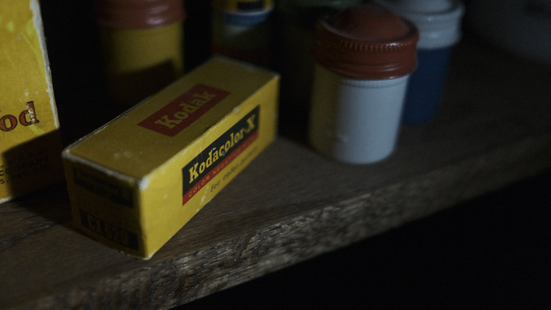 Kodak film box and photography supplies arranged on a wooden shelf with soft natural lighting.