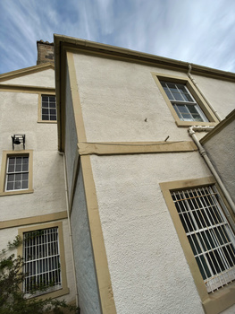 Cream-colored residential building facade with barred windows and tan stone trim against blue sky.