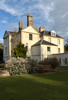 Cream-colored Victorian mansion with multiple chimneys and stone wing, photographed in afternoon light with blue sky.