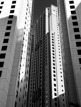 Black and white photograph of tall apartment buildings shot from below, emphasizing vertical lines and geometric patterns.
