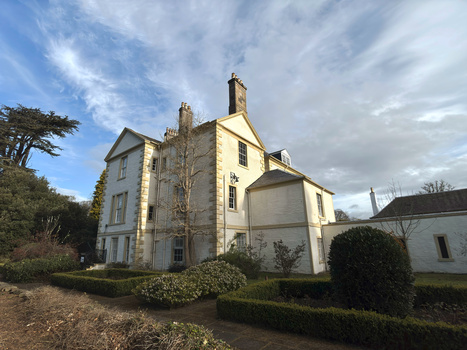 Stone mansion with cream-colored facade and multiple chimneys on a manicured property with blue sky.