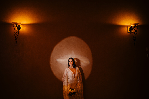 Woman in draped clothing standing before a large circular light with two ornate wall sconces flanking the composition.