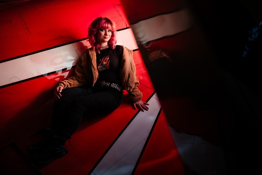 Person seated against red and white geometric backdrop with dramatic red gel lighting.