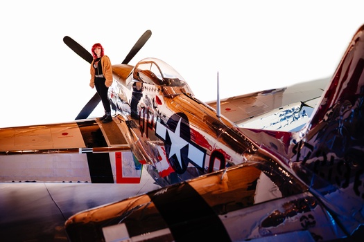 Vintage military aircraft with propeller and nose art, viewed from above with person standing on fuselage.