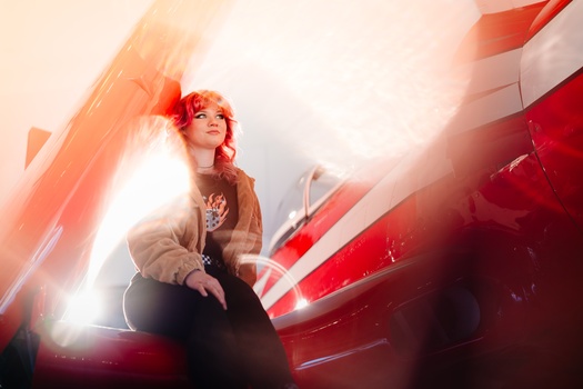 Performer with orange hair under dramatic red and white stage lighting during a concert performance.