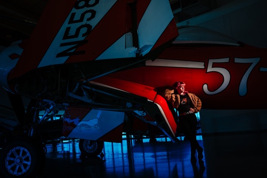Two figures illuminated by red and blue stage lighting, standing beneath a large red panel with numbers, in a theatrical performance setting.