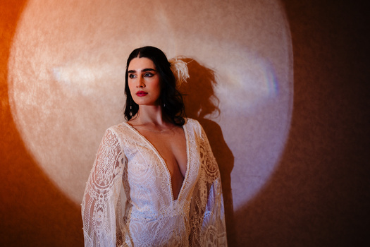Woman in white lace robe against warm-toned circular backdrop with dramatic shadow.
