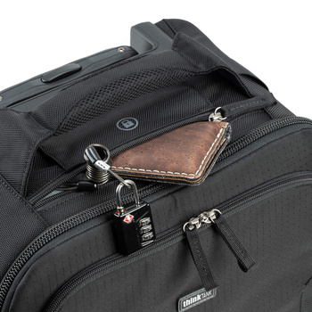 Black camera backpack with brown leather wallet and combination lock attached to exterior zipper.