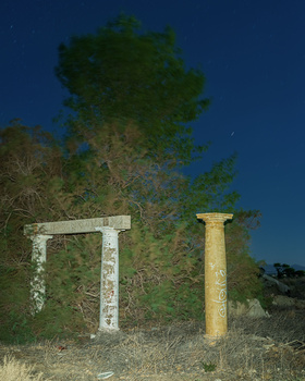 Two weathered concrete pillars standing alone in overgrown vegetation at dusk, framed against a deep blue twilight sky.