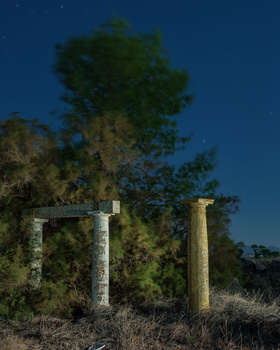 Two concrete pillars stand among overgrown vegetation against a deep blue twilight sky.