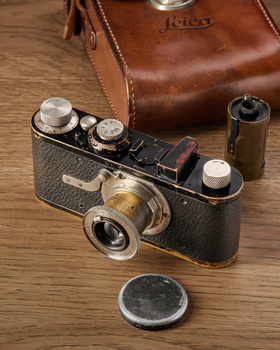 Vintage rangefinder camera with brass lens and black leather body on wooden surface next to brown leather case.