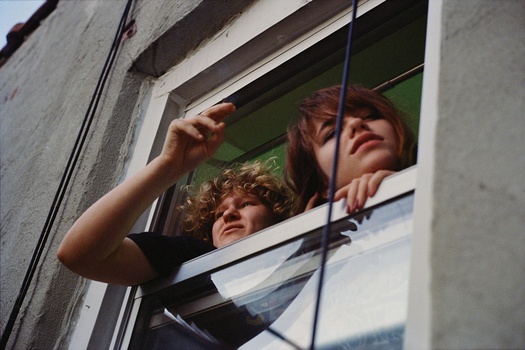 Two people looking out through a window with their hands raised toward the glass panes.