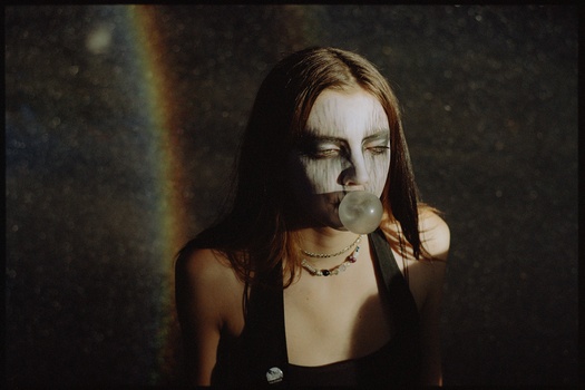 Woman with long dark hair and white face paint against dark background with light refraction.