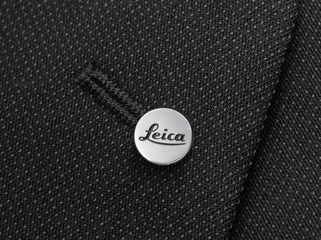 Leica branded pin badge on dark textured fabric with visible stitching detail.