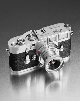 Vintage rangefinder camera with silver top plate and black leather body, photographed against reflective gray surface.