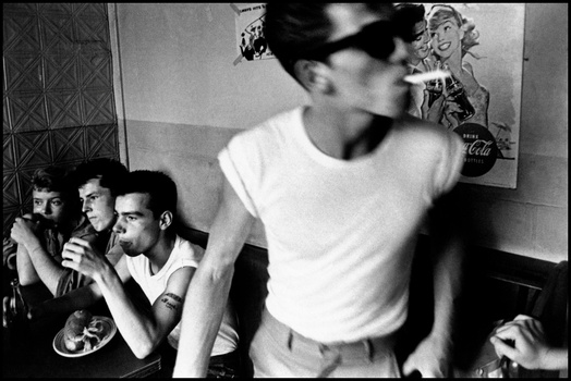 Man in white t-shirt and sunglasses dancing while others watch in an indoor setting.