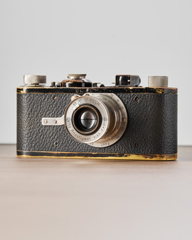 Vintage rangefinder camera with black leather body and brass accents on neutral background.