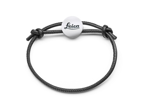 Leica bracelet with dark gray cord and silver circular charm pendant.