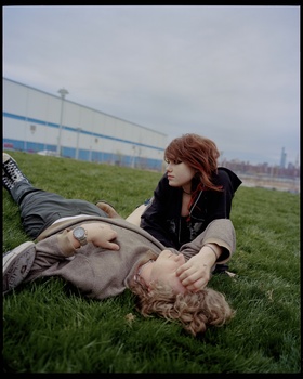 Woman with reddish-brown hair lying on grass, gazing downward in contemplative pose.