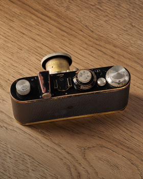Vintage rangefinder camera with leather case and accessories on wooden surface.