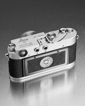 Vintage Leica rangefinder camera with chrome and black leather body, shown from above against dark background.