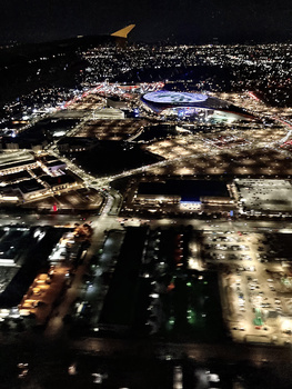 Aerial nighttime photograph of an illuminated stadium complex surrounded by city lights and buildings.