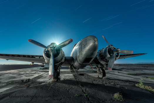 Vintage twin-engine aircraft photographed head-on against a bright sky on a desert runway.