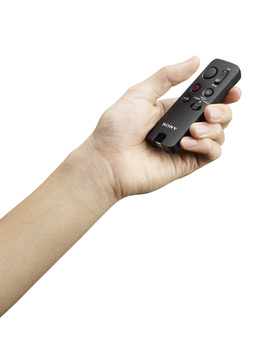 Hand holding a black remote control with multiple buttons and controls.