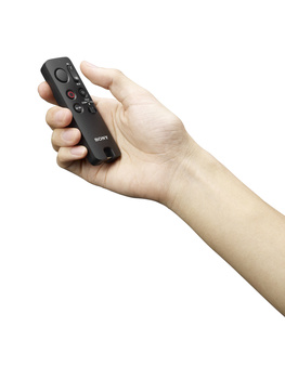 Hand holding a black remote control with buttons and a circular directional pad.