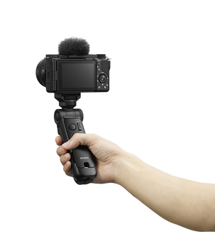 Hand holding a gimbal stabilizer with compact mirrorless camera and microphone mounted on top.