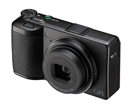 Ricoh GR compact camera with retractable lens and textured grip, shown from three-quarter view against white background.