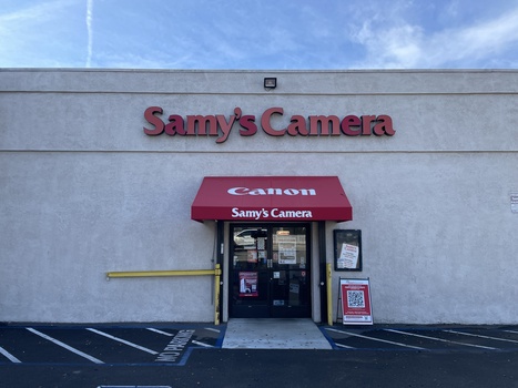 Storefront of Samy's Camera with red awning and signage on white building facade.