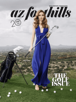 Woman in flowing blue dress holding golf club on hillside with golf bag and landscape background.