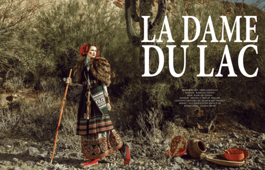Woman in traditional plaid skirt and jacket standing among dried vegetation with hiking gear and rope.