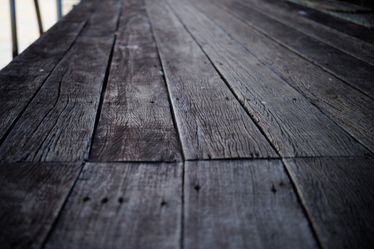 Close-up perspective view of weathered dark wooden deck planks receding into the distance.