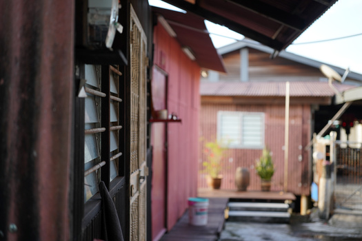 Shallow depth-of-field shot of a dark wooden doorway with a pink building visible in soft focus beyond.