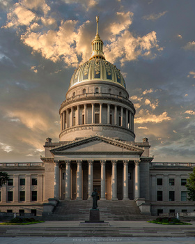 Classical domed government building with columned portico photographed against dramatic golden-hour sky with clouds.